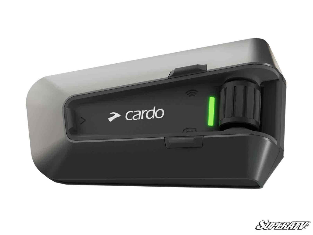 A close-up of the Cardo PACKTALK Edge UTV Communicator, black and silver with a green LED, rotary knob, and Cardo logo on the front. The background is white and features a “SuperATV” watermark in the bottom right corner.