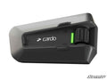 A close-up of the Cardo PACKTALK Edge UTV Communicator, black and silver with a green LED, rotary knob, and Cardo logo on the front. The background is white and features a “SuperATV” watermark in the bottom right corner.