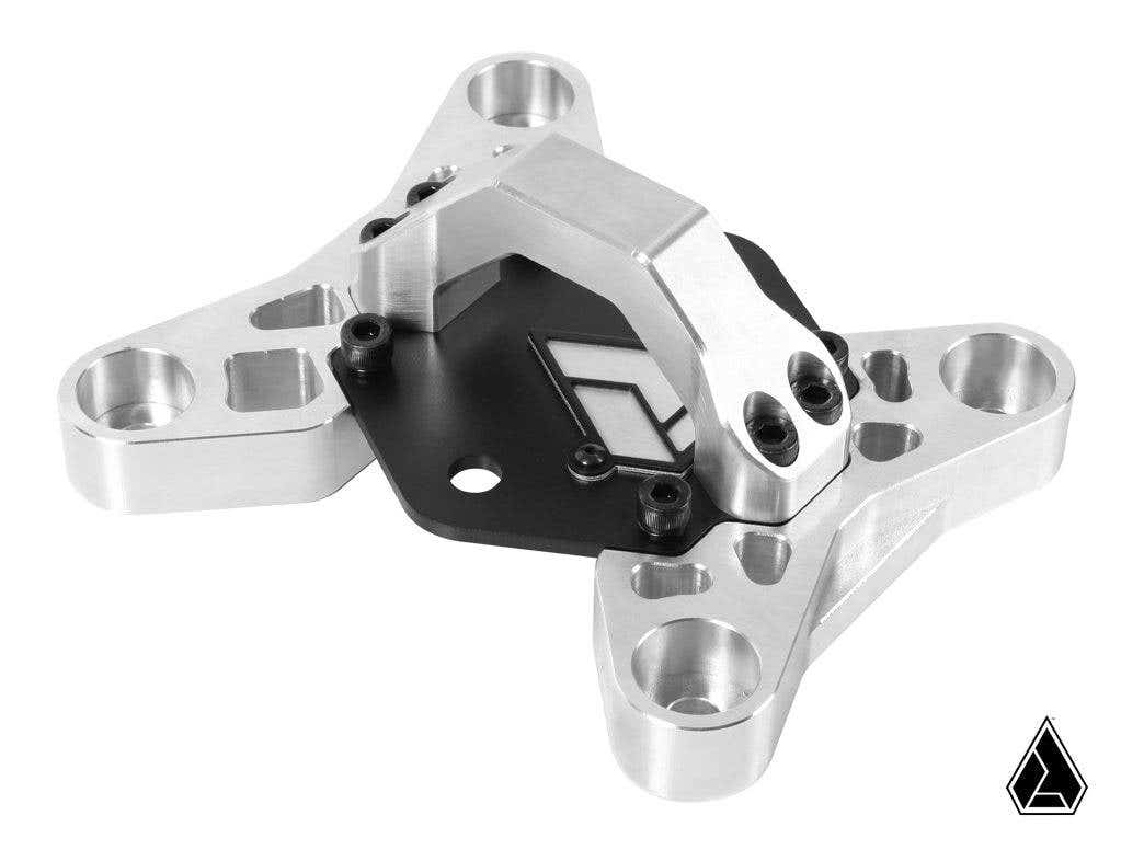 The Assault Industries 3pc Radius Rod Reinforcement Plate for Can-Am Maverick X3 features a machined metal bracket with a triangular base, rounded edges, multiple holes, raised arm, and geometric logo on a black plate, attached by screws.