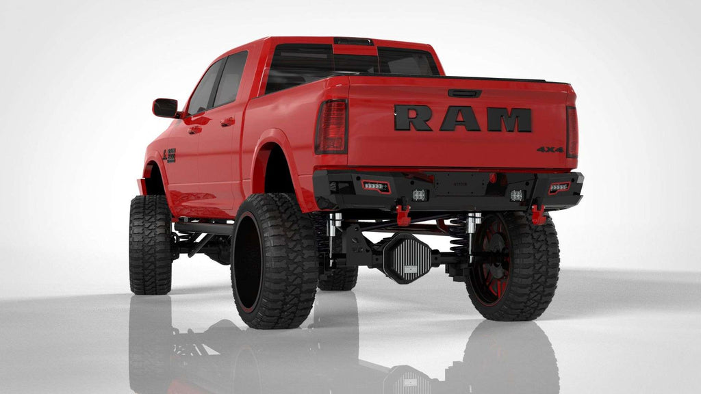 A bright red lifted RAM 2500 4x4 pickup is shown from the rear with oversized off-road tires, black wheels, and a 2010-2018 Ram 2500 Identity Rear Bumper Full Kit (black) featuring shackle end pods, rings, and accent lights.