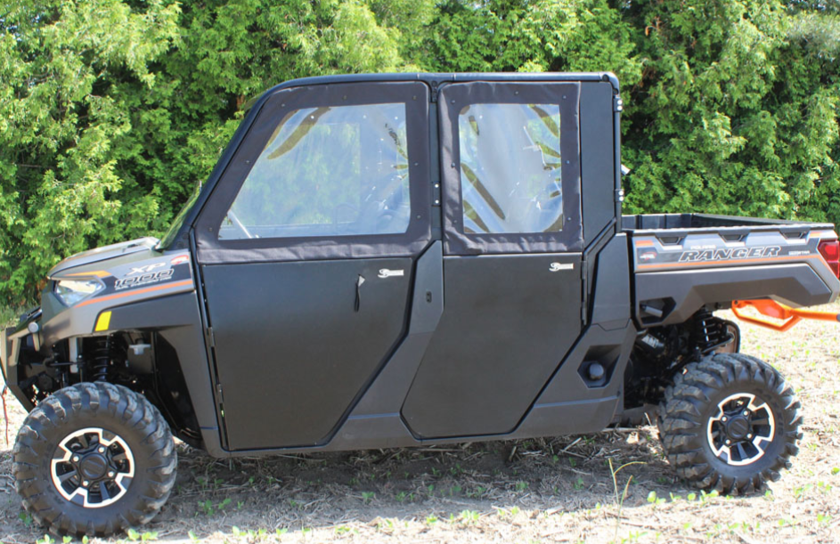 A Polaris Ranger 1000 & XP Crew with Solid Convertible Doors and four enclosed doors is parked on grass in front of green bushes, featuring rugged styling and off-road tires, ideal for outdoor or work environments.