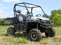 A Polaris Ranger XP equipped with a Polaris Ranger 2 Lift Kit is parked on grass. It’s gray, has two seats, a roll cage, rugged tires, and a rear cargo bed. The SuperATV logo is visible; trees and blue sky are in the background.