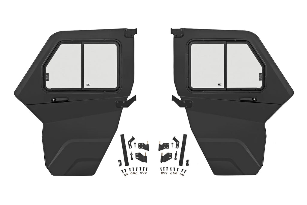 Two black Can-Am Defender Doors for 2 Seater HD 5/7/8/9/10 models are displayed side by side with rectangular windows, alongside neatly arranged mounting hardware and fasteners, showing this is a complete installation kit.