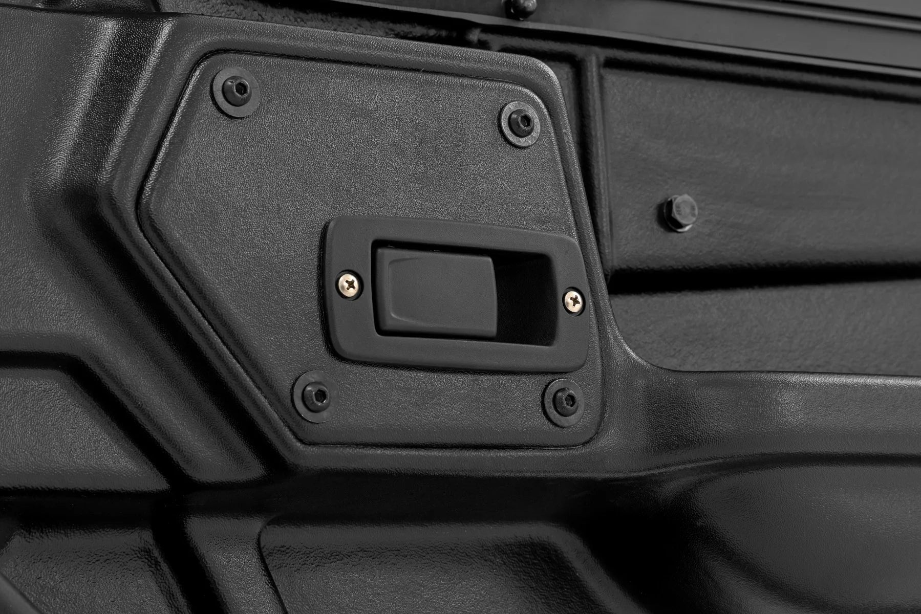 Close-up of a black, textured panel on a 2 Seater | Can-Am Defender Doors HD 5/HD 7/HD 8/HD 9/HD 10, showing a rectangular recessed handle with two visible screws and geometric contours plus four extra screw holes.