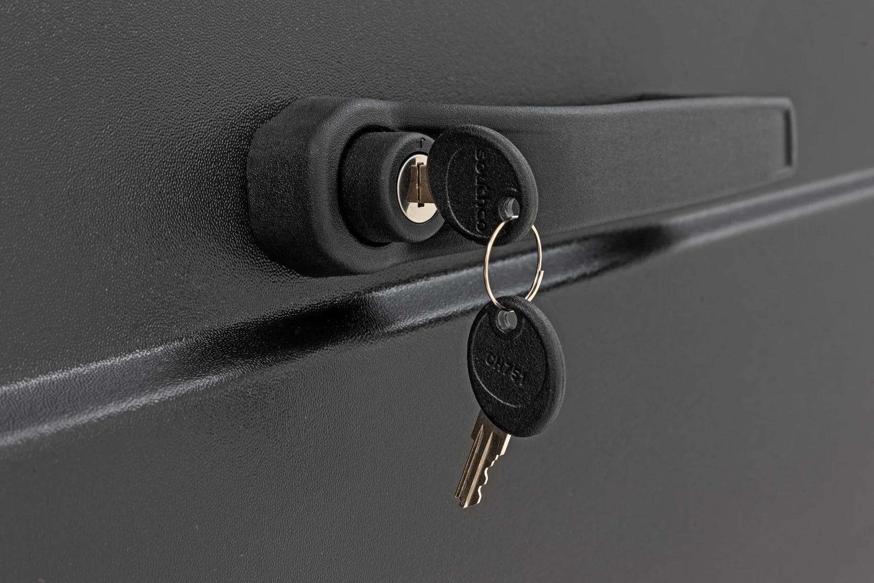 A close-up of a black lockable handle with two keys on a metal ring inserted in the built-in lock cylinder, shown on the matte, textured surface of Can-Am Defender Doors for HD 5/HD 7/HD 8/HD 9/HD 10 (2 Seater).