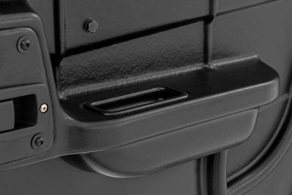 Close-up of a textured black plastic surface on the 2 Seater | Can-Am Defender Doors HD 5/HD 7/HD 8/HD 9/HD 10, showing a shallow rectangular recess, vertical seam, screw, and partial handle—suggesting sturdy equipment enclosure.