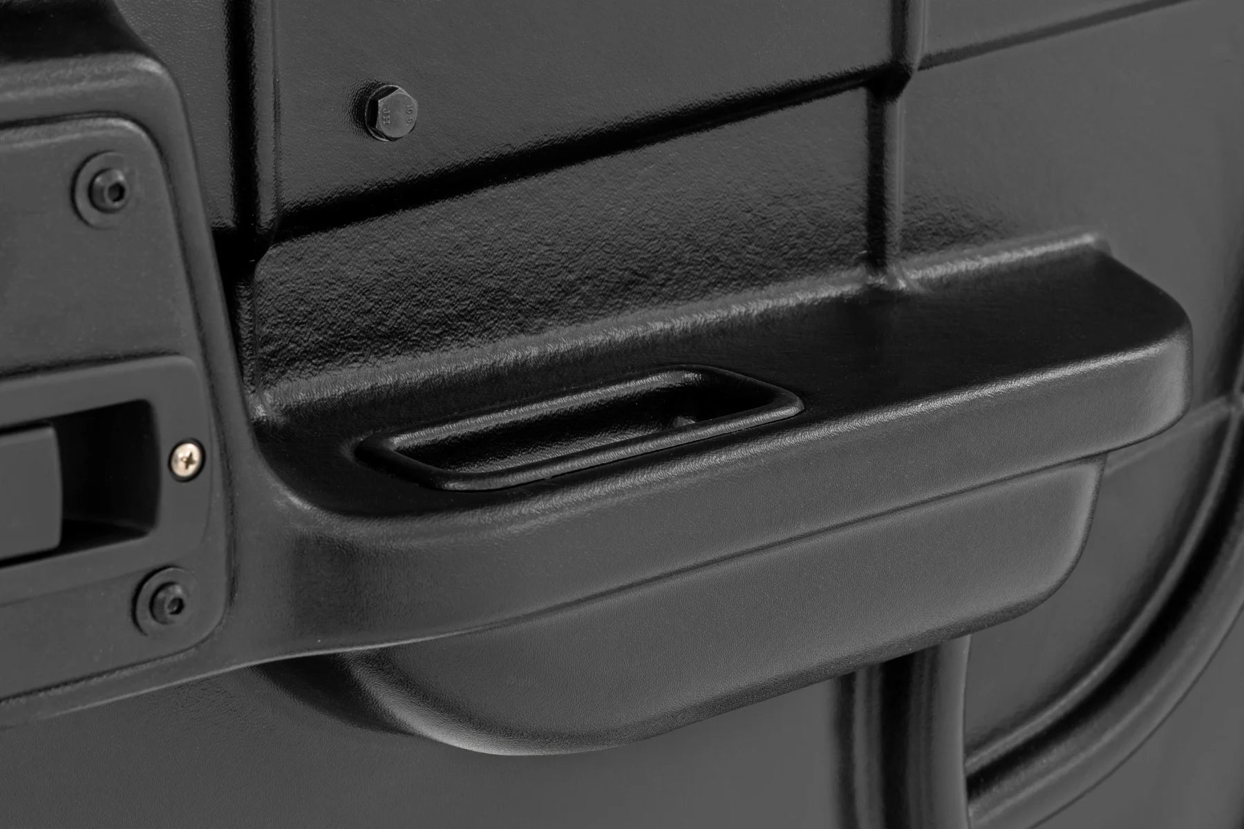 Close-up of a textured black plastic surface on the 2 Seater | Can-Am Defender Doors HD 5/HD 7/HD 8/HD 9/HD 10, showing a shallow rectangular recess, vertical seam, screw, and partial handle—suggesting sturdy equipment enclosure.