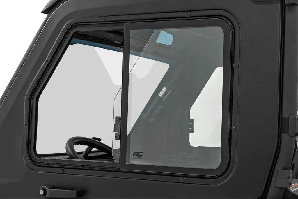 Close-up of a 2 Seater Can-Am Defender’s side window, partially open, featuring a sliding glass panel and black metal frame. The steering wheel and dashboard are visible inside; the matte black exterior is also shown. For HD 5/7/8/9/10 models.