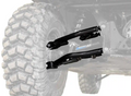 Close-up of Defender HD10 1.5 Rear Offset A-Arms and coil springs on an off-road vehicle, attached to a large, knobby tire. The background and tire are faded to emphasize the upgraded suspension components.