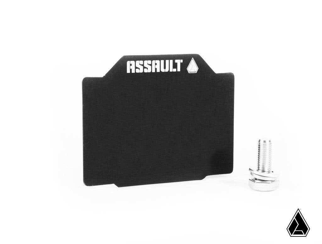 A black metal Assault Industries 4 x 3 UTV Registration Plate with “ASSAULT” and a white triangle logo appears next to a small silver threaded bolt, on a white background with a black triangle logo in the lower right corner.