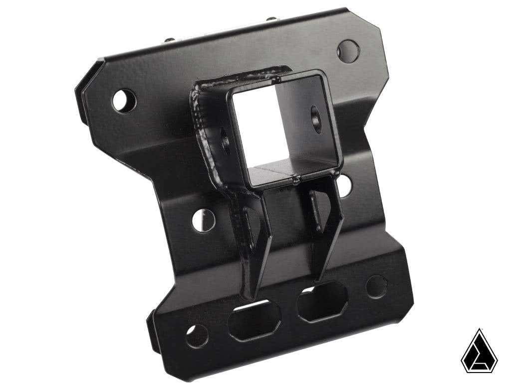 The Assault Industries Heavy Duty Rear Chassis Brace with Tow Hitch for Can-Am Maverick X3 is a black metal bracket featuring a square central opening, multiple screw holes, cutouts, angled edges, raised details, and a triangle logo at the bottom right.