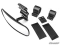The Tracker Rear View Mirror kit includes a black rectangular mirror, a pivot mount, two circular brackets, two rectangular adhesive pads, and mounting plates. All items are displayed neatly on a white background with the SuperATV logo in the corner.
