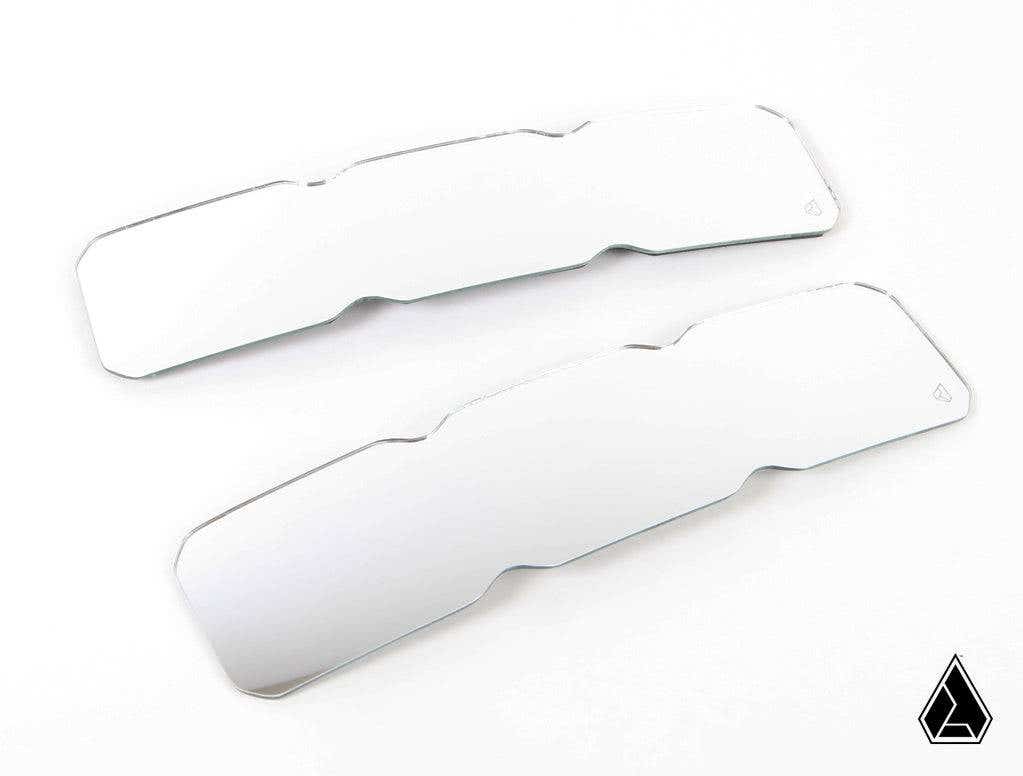 Two identical Assault Industries Bomber Convex Center Mirror Glass Replacement lenses with contoured edges are side by side on a white background, each featuring a small engraved logo, with a geometric black logo at the image’s bottom right.