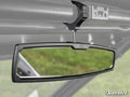 The Kawasaki Mule Pro Aluminum Rear-View Mirror, featuring a black frame and rectangular design, is mounted inside the vehicle on a metal support bar. The blurred green grass background and SuperATV logo appear in the lower right corner.