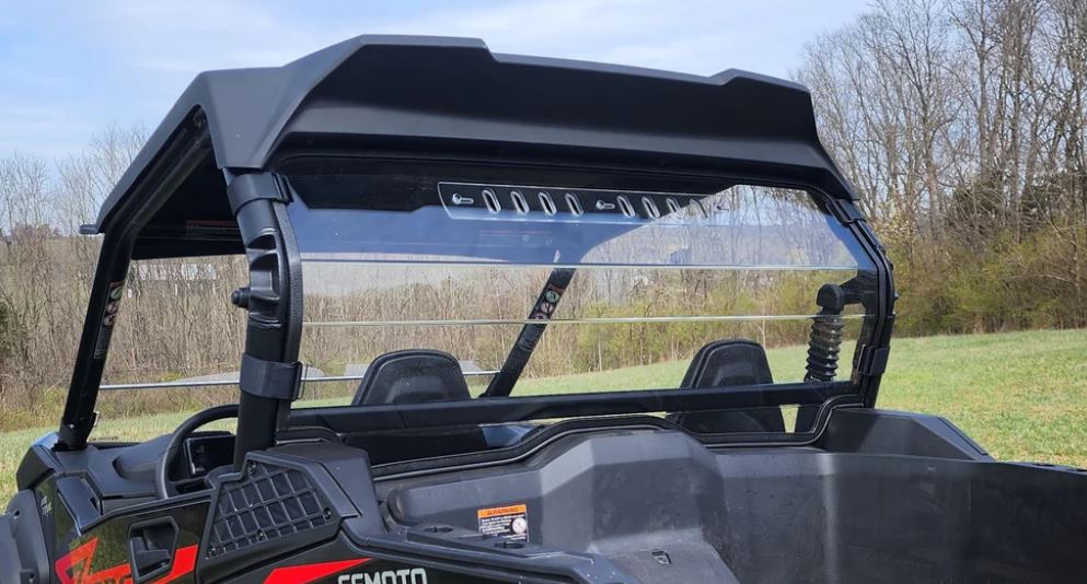 A close-up of the rear side of a black CFMoto ZForce 800 Trail/950 Sport & Trail with a 1 Piece Lexan Back Panel, roll cage, and two seats. The background features a grassy field and leafless trees under a blue sky.
