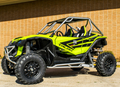 A bright green Honda Talon with S3 Power Sports 2019+ Honda Talon Nerf Bars, black accents, roll cage, large rugged tires, and roof bars is parked on a driveway in front of a tan brick wall. Two bucket seats are visible inside.