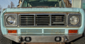 Close-up of the front of an old, weathered light blue International Harvester with a metal grille showing rust, rectangular headlights, and a Front Bumper for International Scout featuring two square LED lights mounted below.