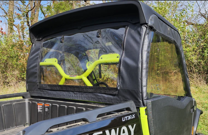 The Segway UT10 - Upper Door/Rear Window Combo is shown installed on a black and green UTV, with clear plastic windows exposing the bright green frame and yellow-green handlebars. The vehicle is parked outside near trees and tall grass.