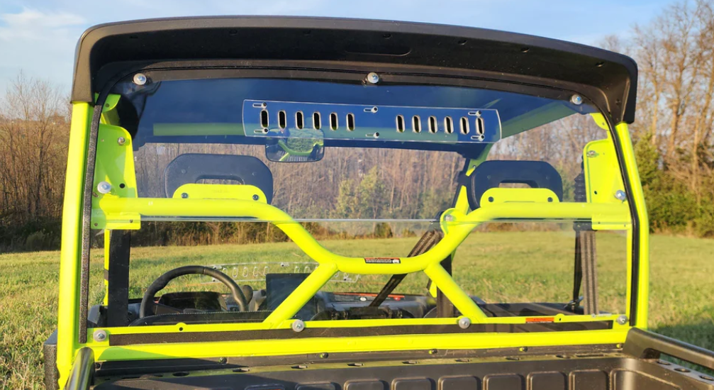 Rear view of a Segway UT10 with a neon yellow roll cage and the Lexan Back Panel for Single Cab installed. The clear panel, featuring a top-center vent and bolt attachments, is set against grassy fields and leafless trees under a blue sky.