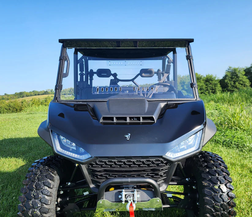 A Segway UT10 Crew with a 1-piece scratch-resistant front windshield featuring vents is parked on green grass, viewed head-on with rugged tires and LED headlights. Trees and a blue sky are in the background.