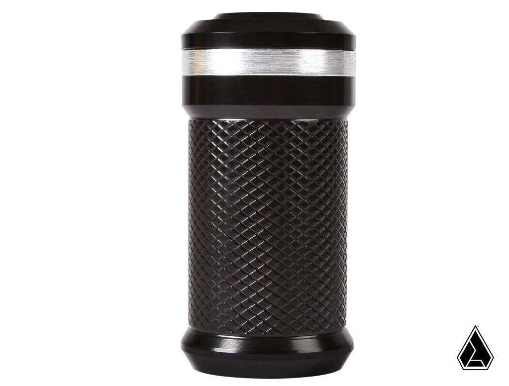 The Assault Industries M2HB Billet Shift Knob for Can-Am Maverick X3 is a black, cylindrical metal knob with a diamond-patterned grip and smooth band near the top. Flat ends, white background, and a small black geometric logo in the bottom right corner.