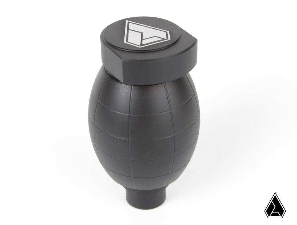 The Assault Industries Assault Army Grenade Shift Knob for Polaris RZR and Ranger is a matte black, grenade-shaped accessory with subtle grooves. It features white geometric logos on the top and bottom right corner, shown against a plain white background.
