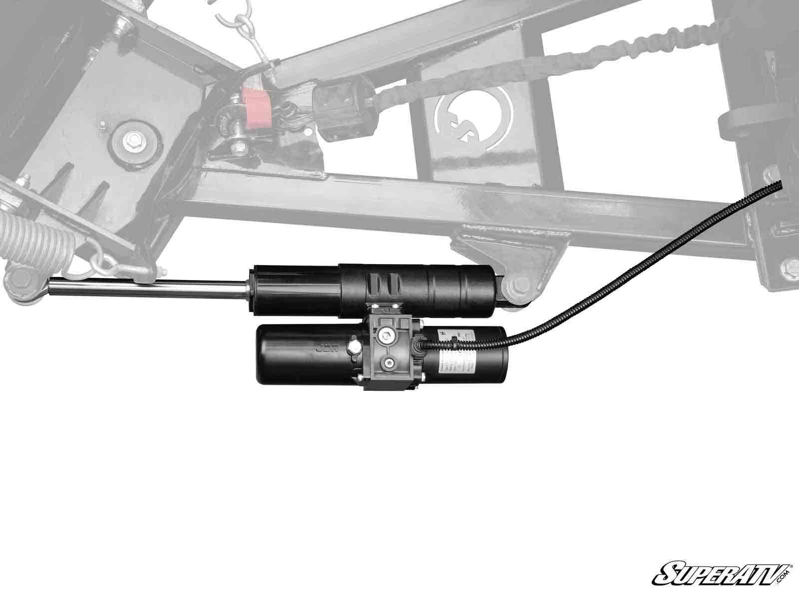 A Plow Pro UTV Plow Angle Actuator Kit in black is shown against a faint grayscale ATV frame background, featuring a cylindrical motor, rods, wiring, and the SuperATV logo in the bottom right corner.