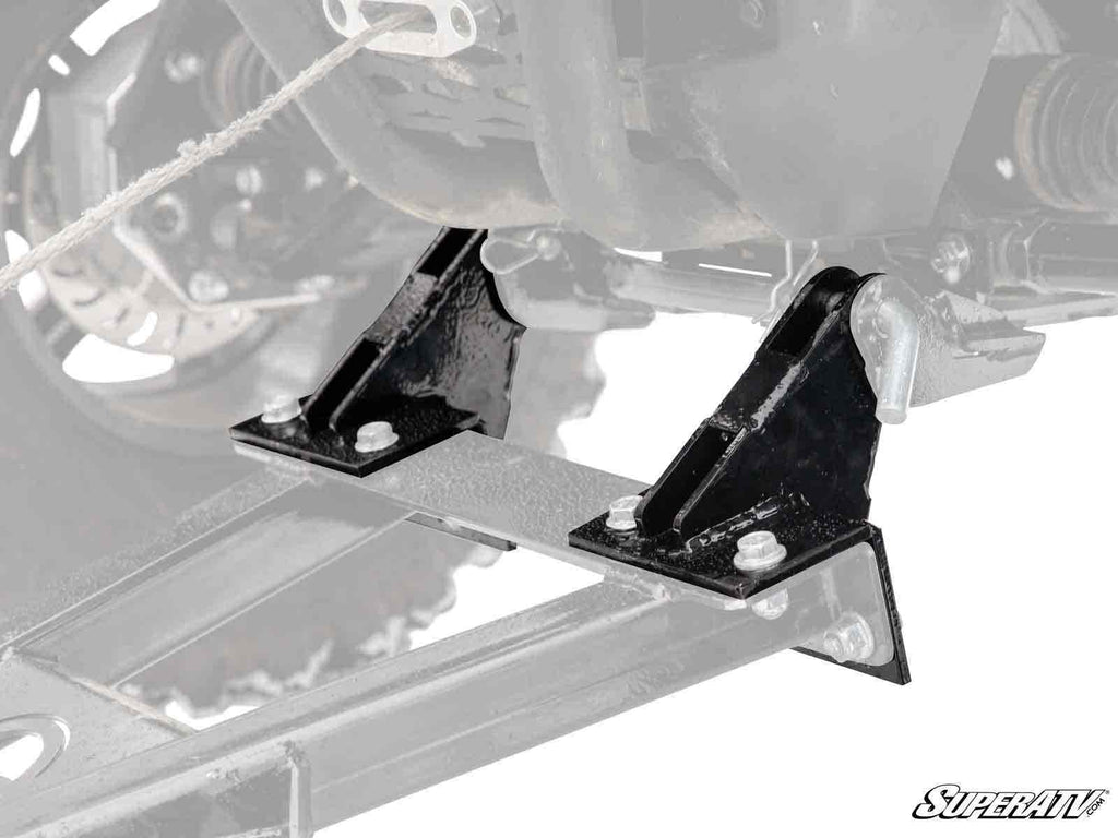 Close-up of sturdy, angular Plow Pro Snow Plow Drop Brackets in black metal, mounted to a vehicle frame with four bolts. The brackets are highlighted against a faded background; SuperATV logo appears in the bottom right corner.