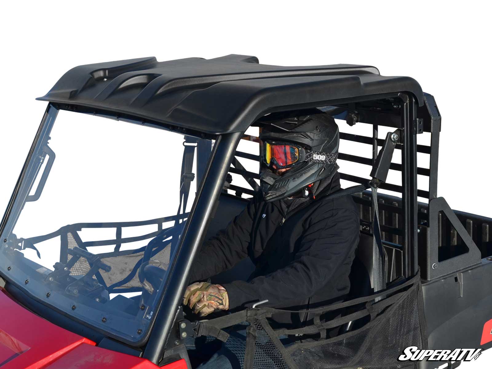 A person wearing a black helmet, goggles, and gloves drives a red off-road vehicle featuring the Polaris Ranger Mid Size 570 Plastic Roof (2015+) with netted doors. The scene has a plain white background and SuperATV branding in the bottom right corner.
