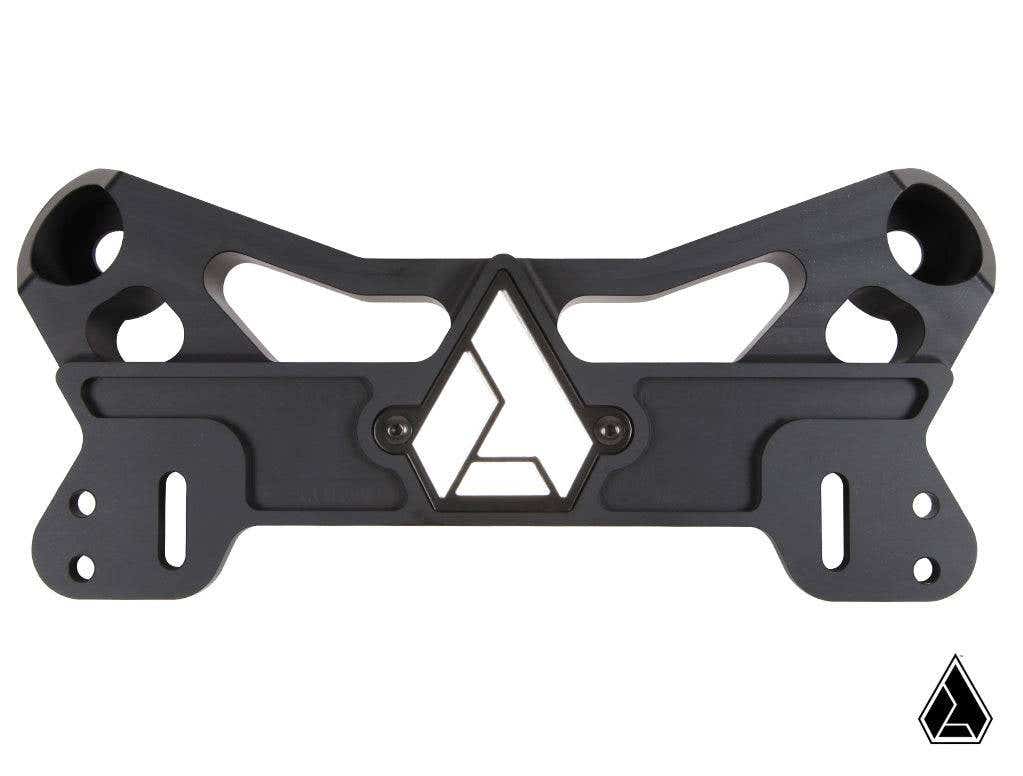 The Assault Industries F-22 Heavy Duty Shock Tower Brace Kit for Can-Am Maverick X3 is a black CNC-machined metal part with angular cutouts, a central geometric triangle logo, multiple mounting holes, and smooth edges on a white background.