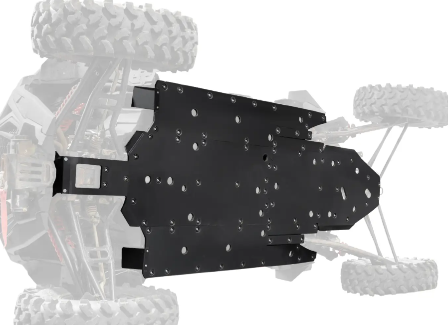 A close-up, top-down view shows a Polaris RZR XP 4 Turbo S Full Skid Plate—a black metal, rectangular, hole-punched plate mounted on the vehicle’s underside, with the rest of the off-road vehicle blurred in the background.