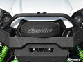 Close-up of a white off-road vehicle’s front bumper with a black SuperATV Winch Cover featuring the “SuperATV.com” logo, rugged diamond-plate texture, visible green suspension springs, and part of the “SuperATV” logo in the corner.