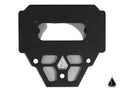 The Assault Industries Switch Pro Steering Wheel Mount is a black metal plate with geometric cutouts, several circular holes, and a large top rectangular opening. The Assault Industries emblem appears twice on the lower right against a white background.