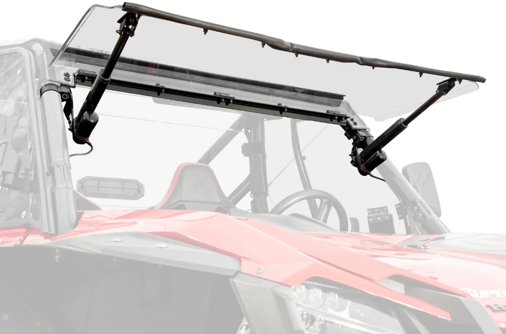 A close-up of a Honda Talon 1000 Max-Drive Power Flip Windshield, shown clear and upward-tilted with black brackets. The vehicles frame, steering wheel, and seat are visible beneath the partially raised windshield against a white background.