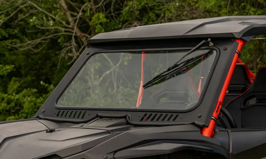 Close-up of a Honda Talon 1000 featuring its Glass Windshield, single wiper blade, and orange roll bars. The off-road vehicle is parked outdoors with green leafy trees in the background on a sunny day.