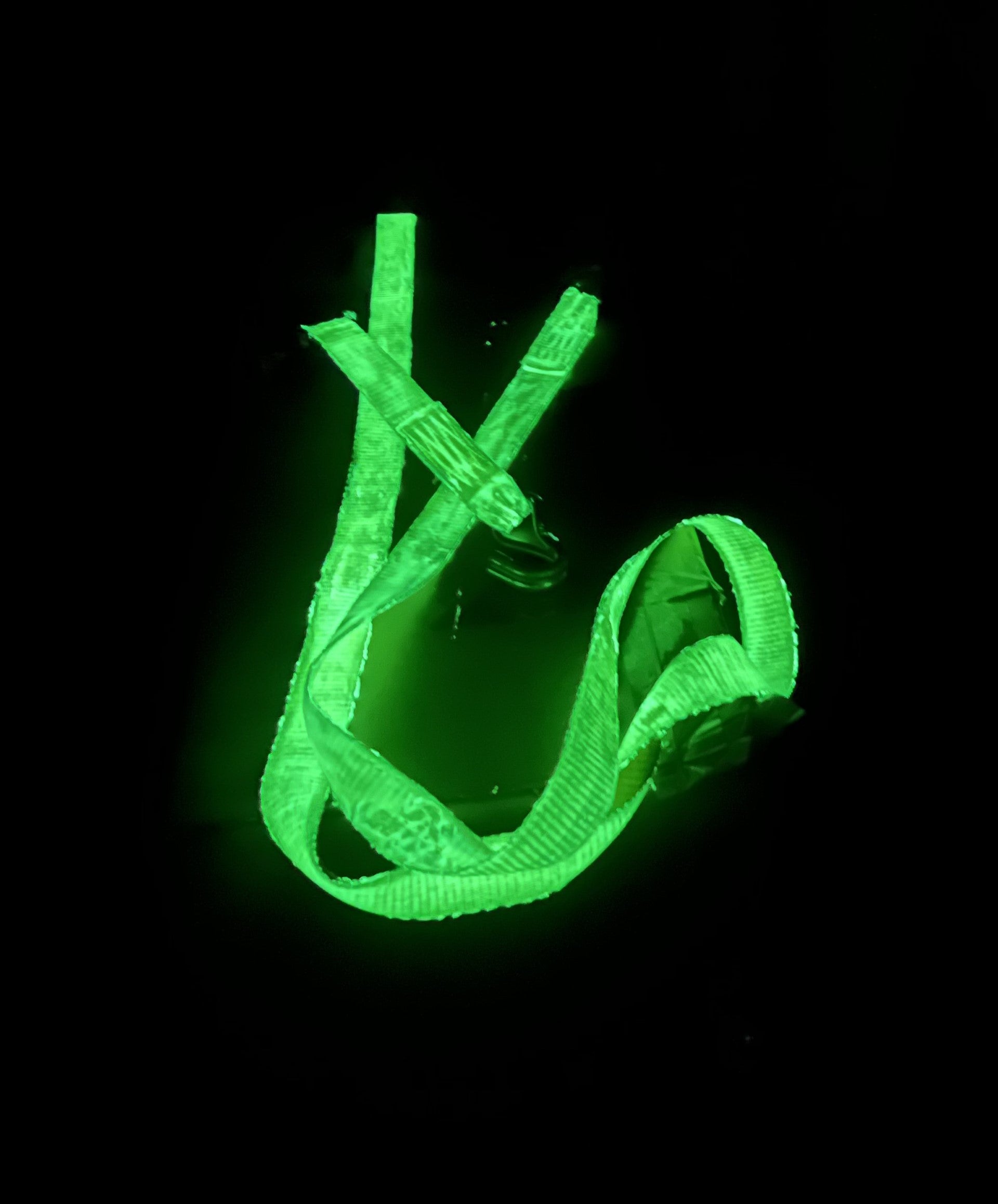 The GLOSTRAP, the world’s first glow-in-the-dark ratchet strap, glows bright green against a black background, partially coiled so its luminescent material is clearly visible.