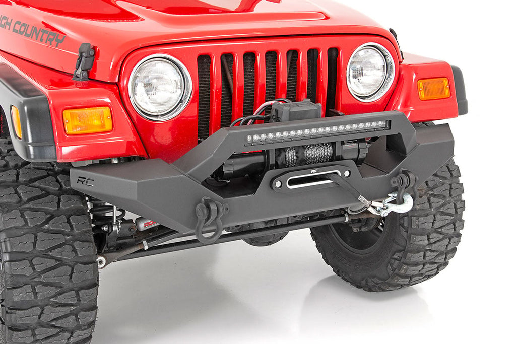 A close-up of a red Jeep Wrangler TJ (1997-2006) with the Rough Country Front Bumper Rock Crawler, featuring a mounted winch, D-ring shackles, light bar, rugged tires, round headlights, and visible front grille.