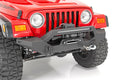 A close-up of a red Jeep Wrangler TJ (1997-2006) with the Rough Country Front Bumper Rock Crawler, featuring a mounted winch, D-ring shackles, light bar, rugged tires, round headlights, and visible front grille.