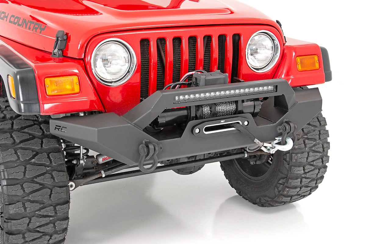 A close-up of a red Jeep Wrangler TJ (1997-2006) with the Rough Country Front Bumper Rock Crawler, featuring a mounted winch, D-ring shackles, light bar, rugged tires, round headlights, and visible front grille.