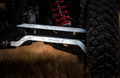 Close-up of Polaris RZR XP Turbo S High Clearance Billet Aluminum Radius Arms in an off-road suspension system, featuring red coil springs, metallic shock absorbers, and a rugged tire outdoors on dry grass.