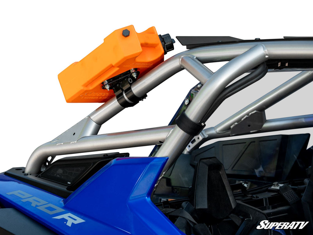 A Universal Jerry Can Cage Mount holds a bright orange fuel canister to the silver roll cage of a blue off-road vehicle above the passenger area. Black mounting hardware, interior details, and the “SuperATV” logo are also visible.