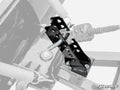 A close-up of the Plow Pro Adjustable Plow Lever Kit’s black metal lock pin mechanism attached to a steel frame with springs and bolts. The shiny, perforated lock stands out against a desaturated background, with the SuperATV logo in the corner.