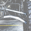 Close-up of S3 Power Sports 2019+ Honda Talon X HD Billet Aluminum Radius Rods, High Clearance Lower, attached to the frame and large off-road tire. The shiny silver rods stand out amid a desaturated background and visible yellow parking lines below.