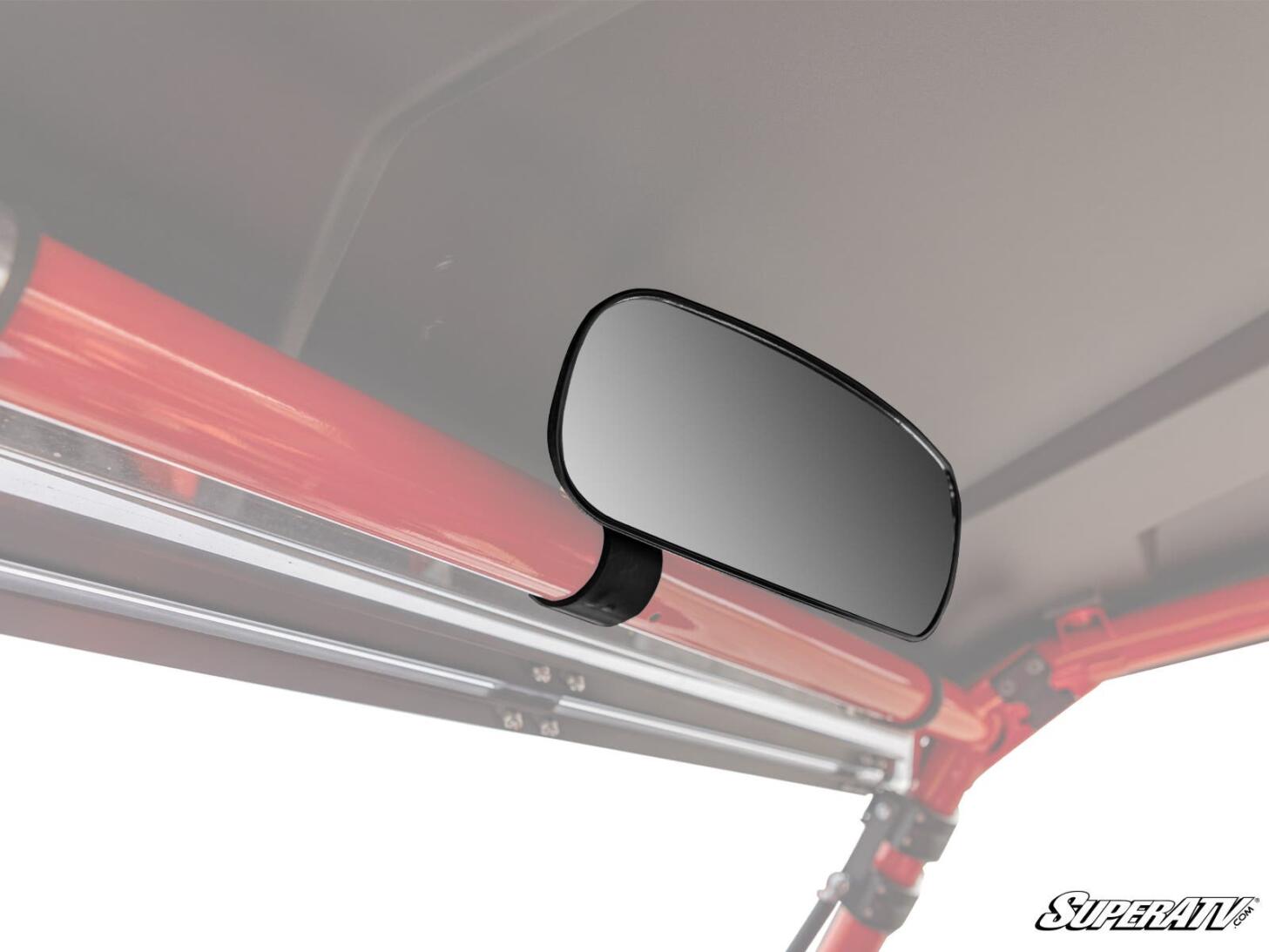 The Can-Am Rear View Mirror is mounted inside a vehicle with a red tubular frame, attached to the roof support bar. It reflects a white background, and the SuperATV logo appears in the bottom right corner.