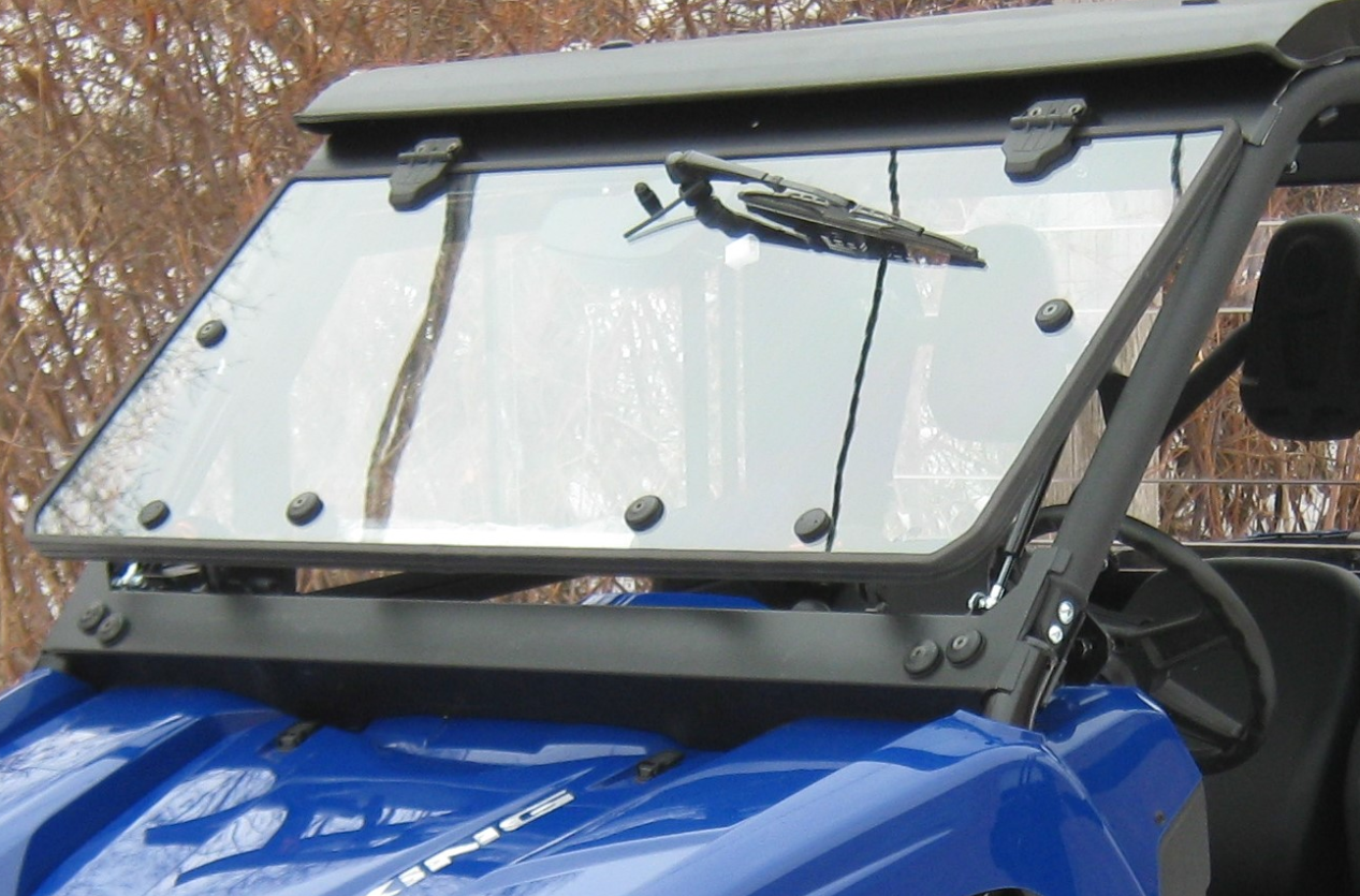 A close-up of the Full Windshield Kit – Yamaha Viking/Viking VI shows its clear tilting glass, right-side mounted wiper, and black fasteners. Bare tree branches appear in the background.