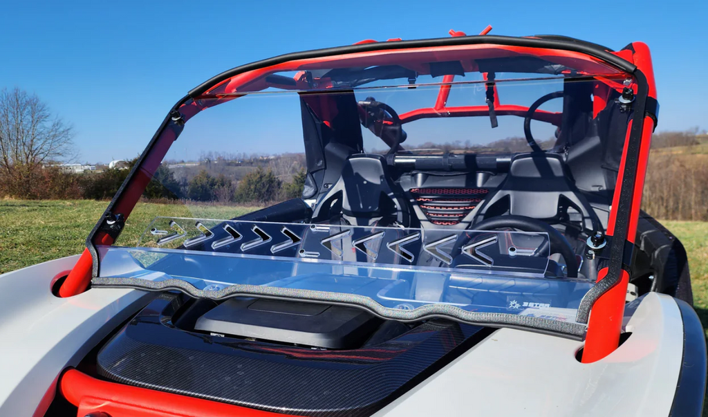 A sporty Segway Villain with a scratch-resistant windshield featuring clamp and vent options is shown parked on grass. The red frame, black seats, and clear angular windshield highlight its futuristic, lightweight design against a scenic backdrop.