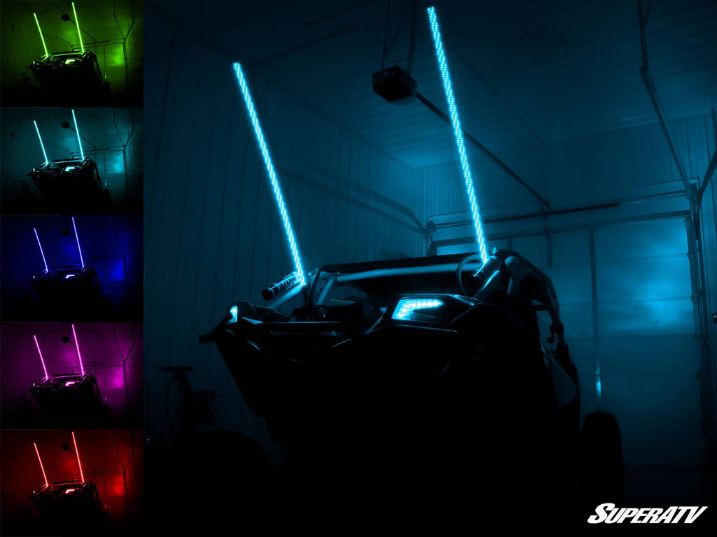 A four-wheeled off-road vehicle in a dark garage displays two blue-glowing RGB LED Whip Lights. On the left, five smaller images show the whips in white, red, green, purple, and yellow. The SuperATV logo is at the bottom right.