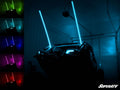 A four-wheeled off-road vehicle in a dark garage displays two blue-glowing RGB LED Whip Lights. On the left, five smaller images show the whips in white, red, green, purple, and yellow. The SuperATV logo is at the bottom right.