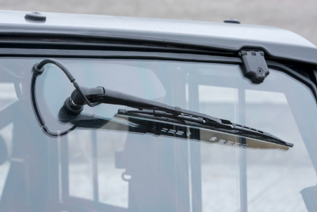 Close-up of the Wiper / Washer Kit for CF Moto UForce 1000, showing the wiper arm and blade on the windshield. The blurred background emphasizes the clear glass and detailed wiper assembly.