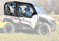 A YAMAHA Wolverine X-4 door kit with black, zippered soft doors and windows is installed on a white side-by-side ATV parked on grass, backed by forest trees. The ATV features large off-road tires and a rugged exterior.